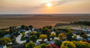 Drone photo looking west in Henderson, Nebraska with houses, ballfield and a corn field in the picture. The sun is setting on a fall day.