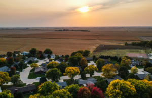Henderson’s West Addition Ensures Room to Grow Drone photo looking west in Henderson, Nebraska with houses, ballfield and a corn field in the picture. The sun is setting on a fall day.