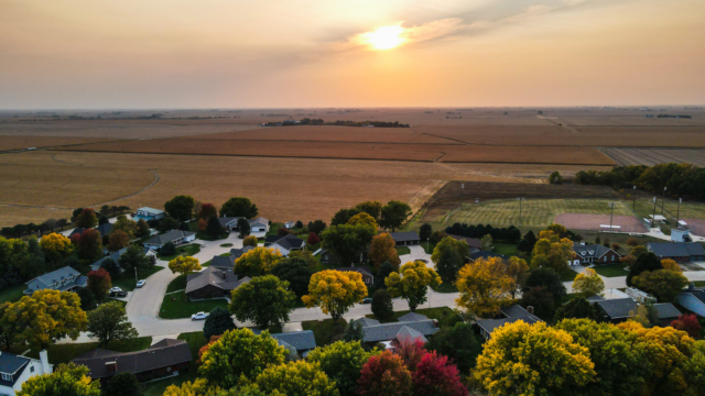 Drone photo looking west in Henderson, Nebraska with houses, ballfield and a corn field in the picture. The sun is setting on a fall day.